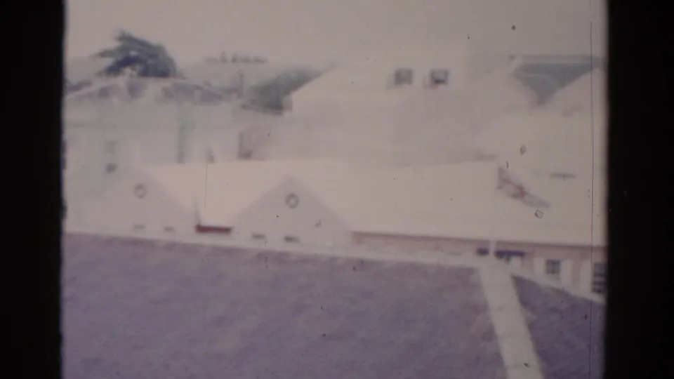 1975 Florida 8mm frame with overexposed white rooftops, a pitched-roof foreground, windows, and trees in the background.
