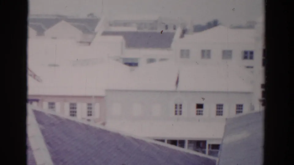 1975 Florida home-movie frame showing pale street-front buildings, rooftops, and dark window or film-frame borders.