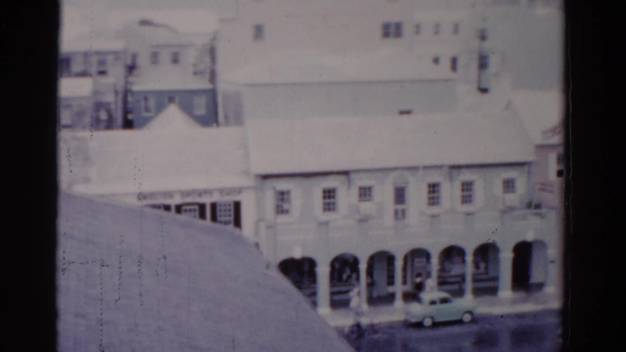 1975 Florida street view with arched ground-floor walkways, pale buildings, a small car, and soft 8mm film texture.