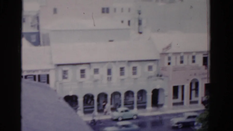 1975 Florida home-movie frame showing arched walkways, cars, pedestrians, and pale street-front architecture.
