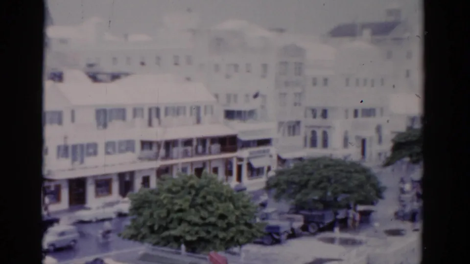 Soft 1975 Florida street frame with white commercial buildings, tree canopy, cars, and storefront details near a corner.