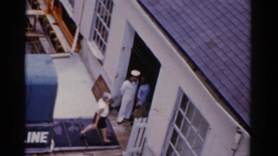 1975 Florida waterfront entrance with a sailor in white, another person in the doorway, and pedestrians passing beneath the Bermuda Line sign.
