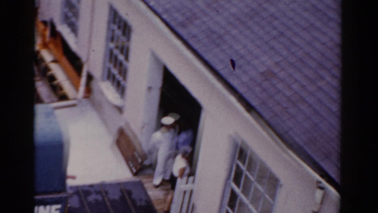 Sailor and adults entering a white waterfront building near a dock.