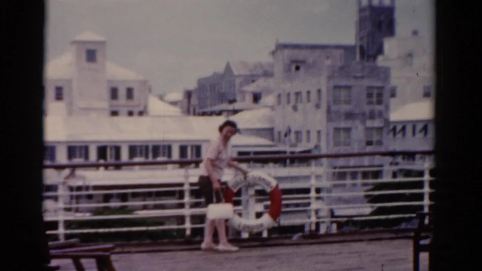 An adult woman pauses beside a white railing and red life preserver on a Florida cruise or dock deck in 1975 home-movie footage.