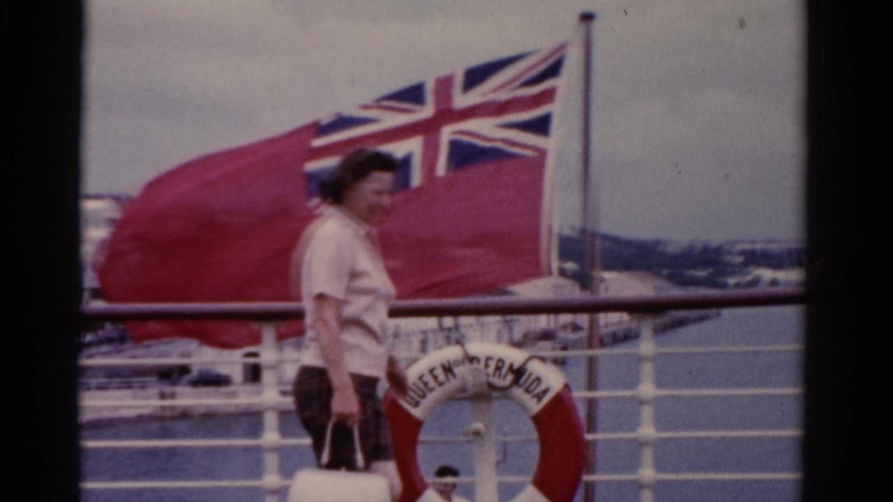 In 1975 Florida footage, a woman walks on a ship deck beside white railings, a British Red Ensign, and a QUEEN OF BERMUDA life preserver.