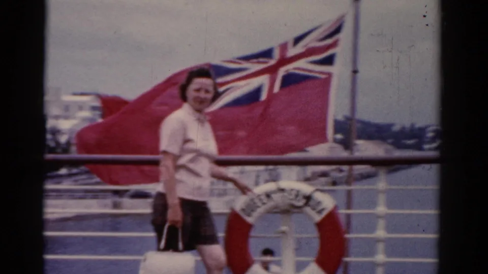 A woman stands on a Florida ship deck in 1975, smiling near a red-and-white life preserver as a British Red Ensign fills the background.