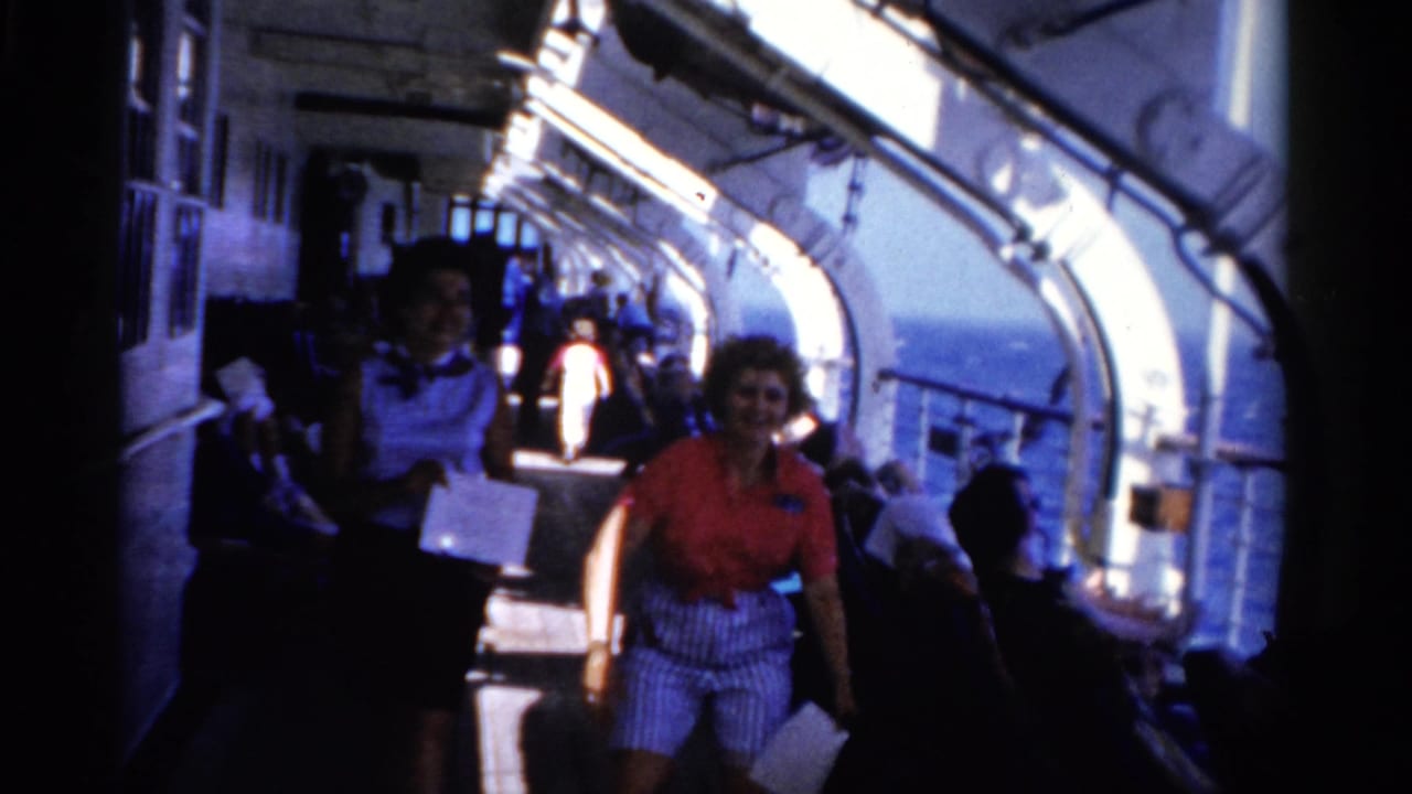 Two smiling women move closer on a 1975 Florida cruise ship deck, with seated passengers and blue sea visible behind them.