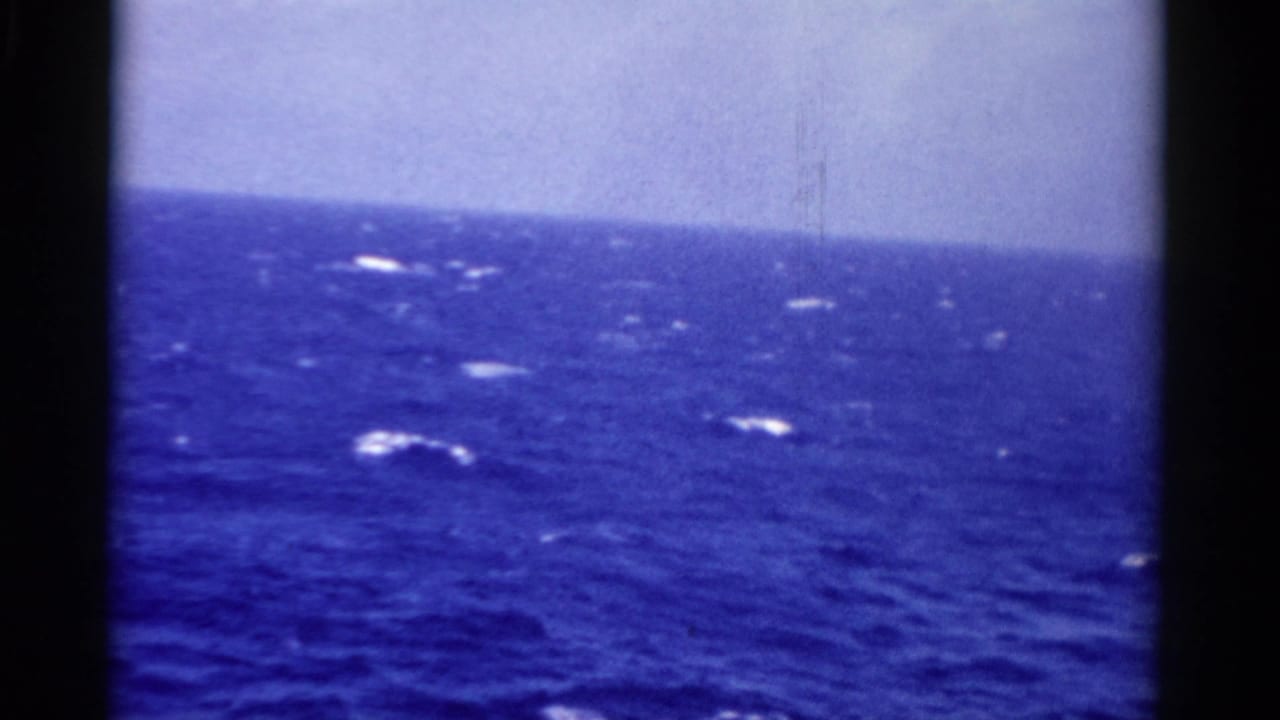 Deep blue ocean with whitecaps under a pale sky, framed by dark film borders.