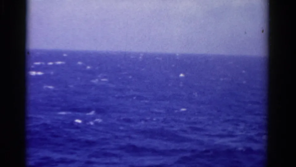1975 Florida home-movie frame of open ocean from a moving vessel, with pale sky, whitecaps, and film gate edges.