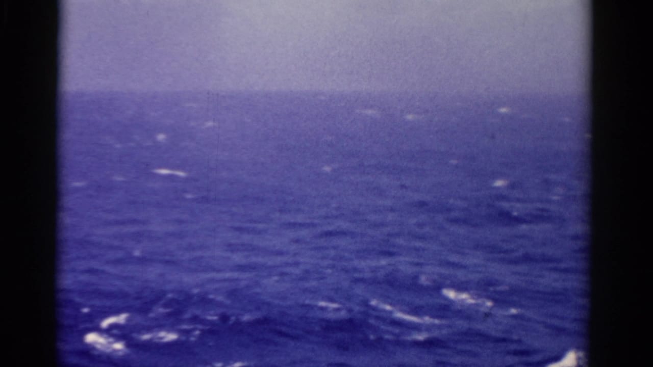 Open ocean with whitecaps and a hazy horizon seen through dark film-frame edges.