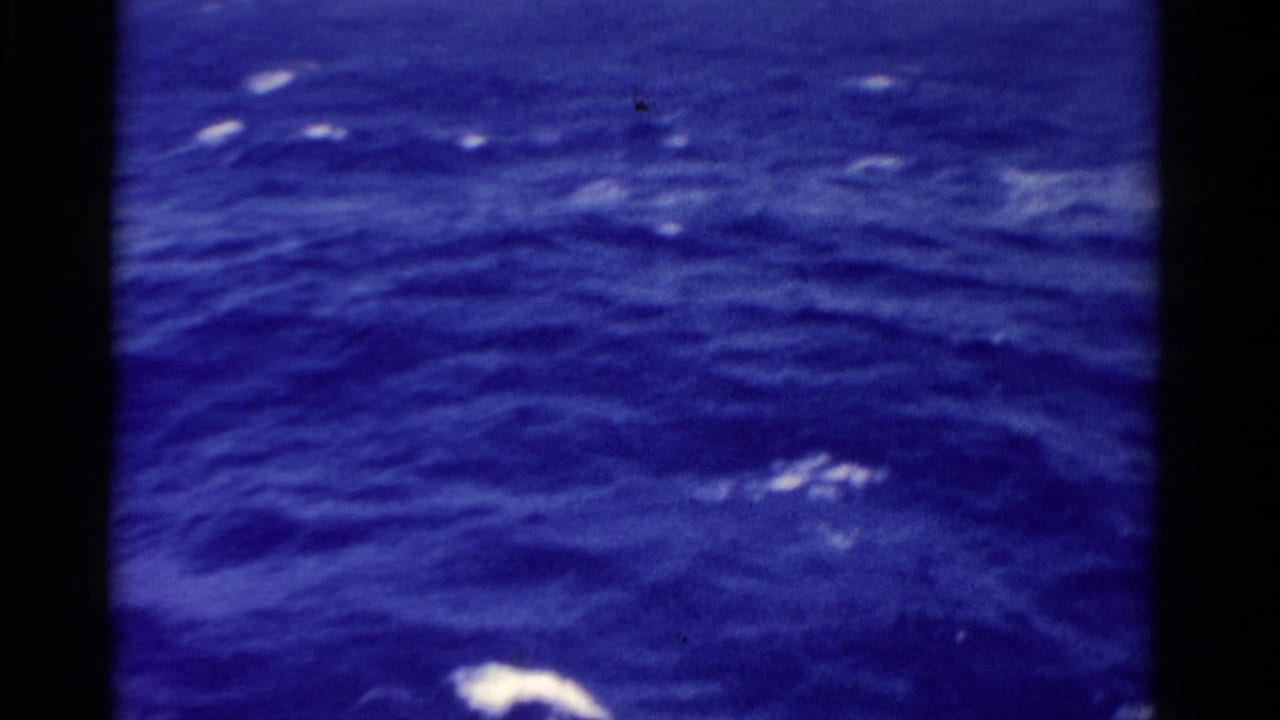 Deep blue ocean surface with small white foam patches and dark film-frame edges.