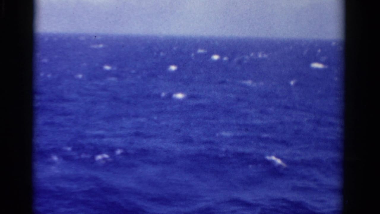 Open sea under a pale sky with bright sun reflections on the water.