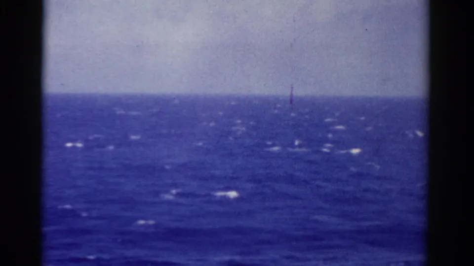 1975 Florida 8mm frame showing a low horizon over blue sea, with small bright reflections and a faint vertical mark near center.