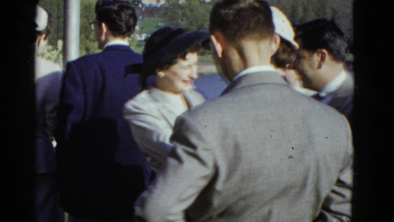A woman in a dark hat smiles among suited men and other adults outdoors.