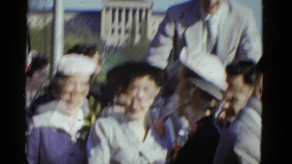 Soft-focus 1975 Boston 8mm frame of adults in dress hats and suits gathered closely outdoors, with motion blur from the handheld camera.