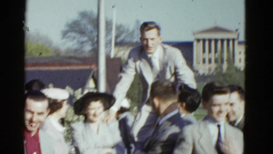 A man in a light suit rises above a group of formally dressed adults during a 1975 Boston outdoor gathering.
