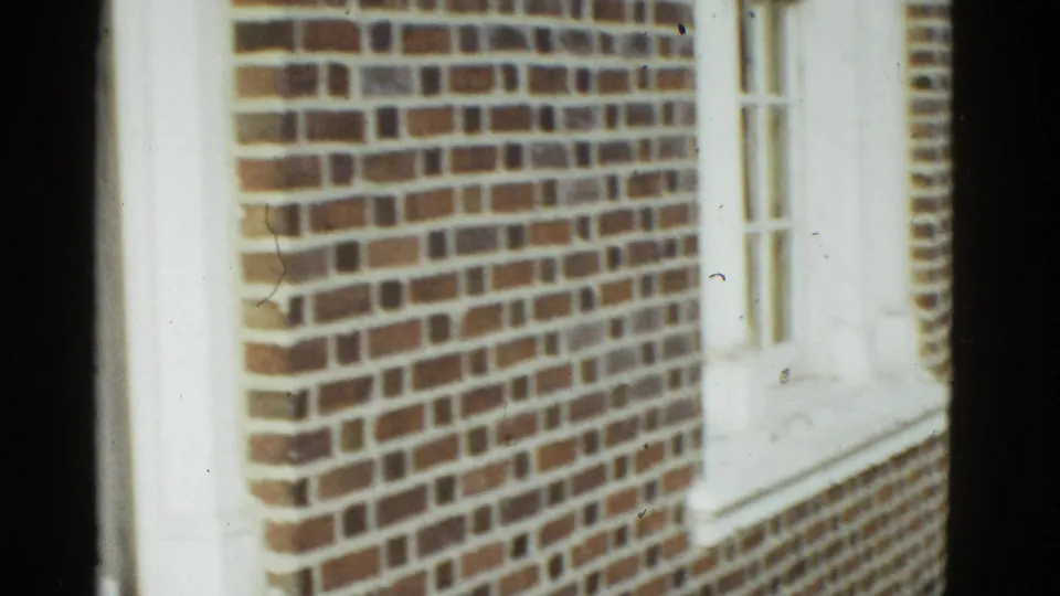 Brick building exterior with white trim appears in the 1975 Boston clip, with the frame partly blocked by dark film edge or camera framing.
