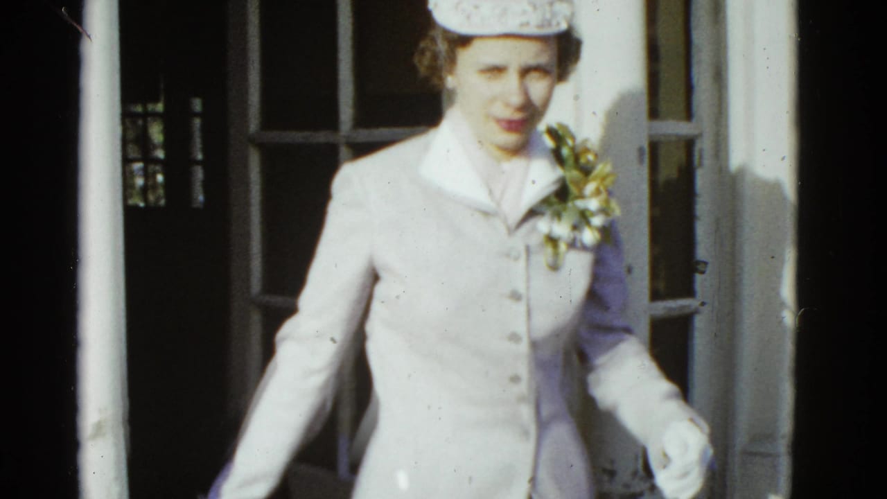 Woman in a light suit and hat steps out through a brick doorway.