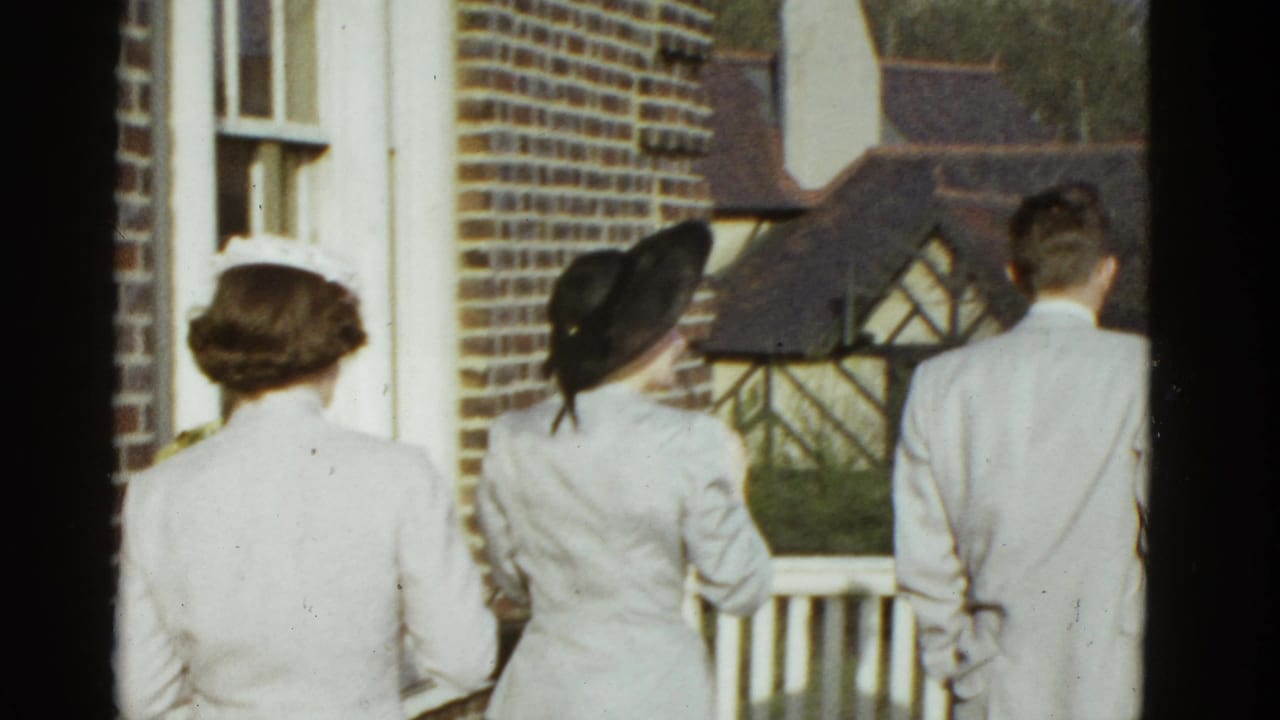 Three adults walk toward a white balcony railing beside a brick house.