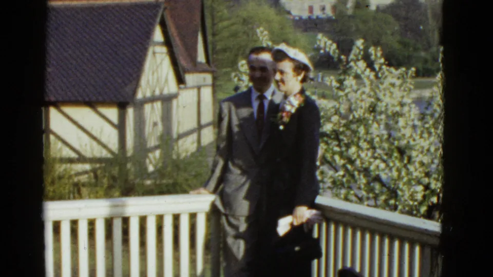 The final frame shows the dressed-up couple still facing the camera on a white-railed balcony in metadata-supported 1975 Boston.