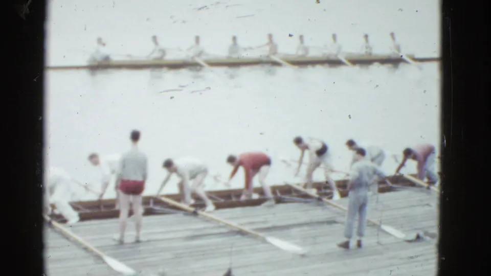 At a Boston rowing site in 1975 home-movie footage, crew members prepare rowing shells on a dock as another boat moves across calm water.