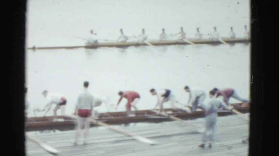 Crew members in vintage athletic clothing adjust rowing shells and oars on a wooden dock during 1975 Boston home-movie footage.