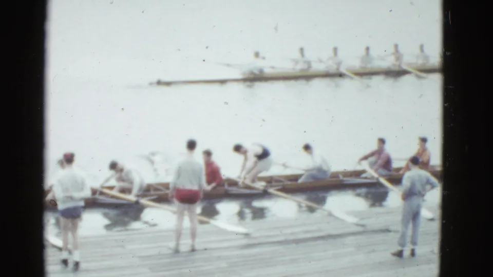 In the final 1975 Boston frame, rowers gather around shells on a wooden dock while a distant crew rows across the bright water.
