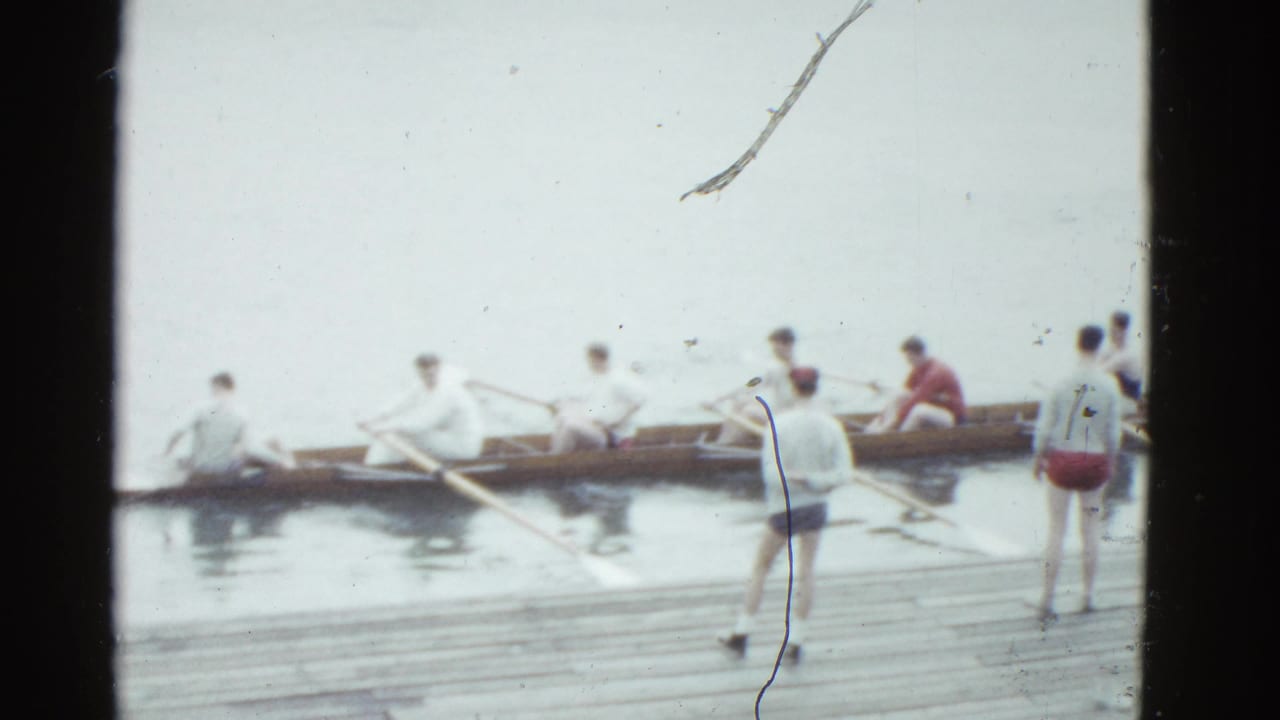 Long rowing shell beside the dock with several rowers holding oars in the water.