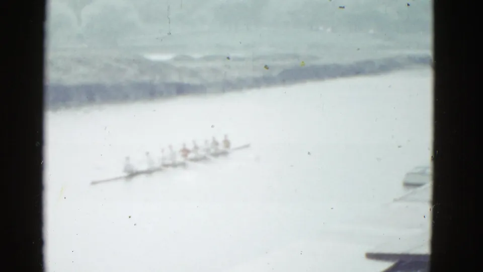 A wider, softer 8mm view shows the rowing crew farther away on the river, with shoreline detail and a partial object at right.