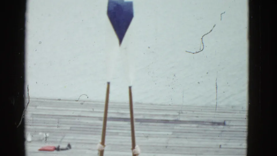 A cropped 8mm frame shows the pole structure and dock surface, with pale water and film scratches across the scene.