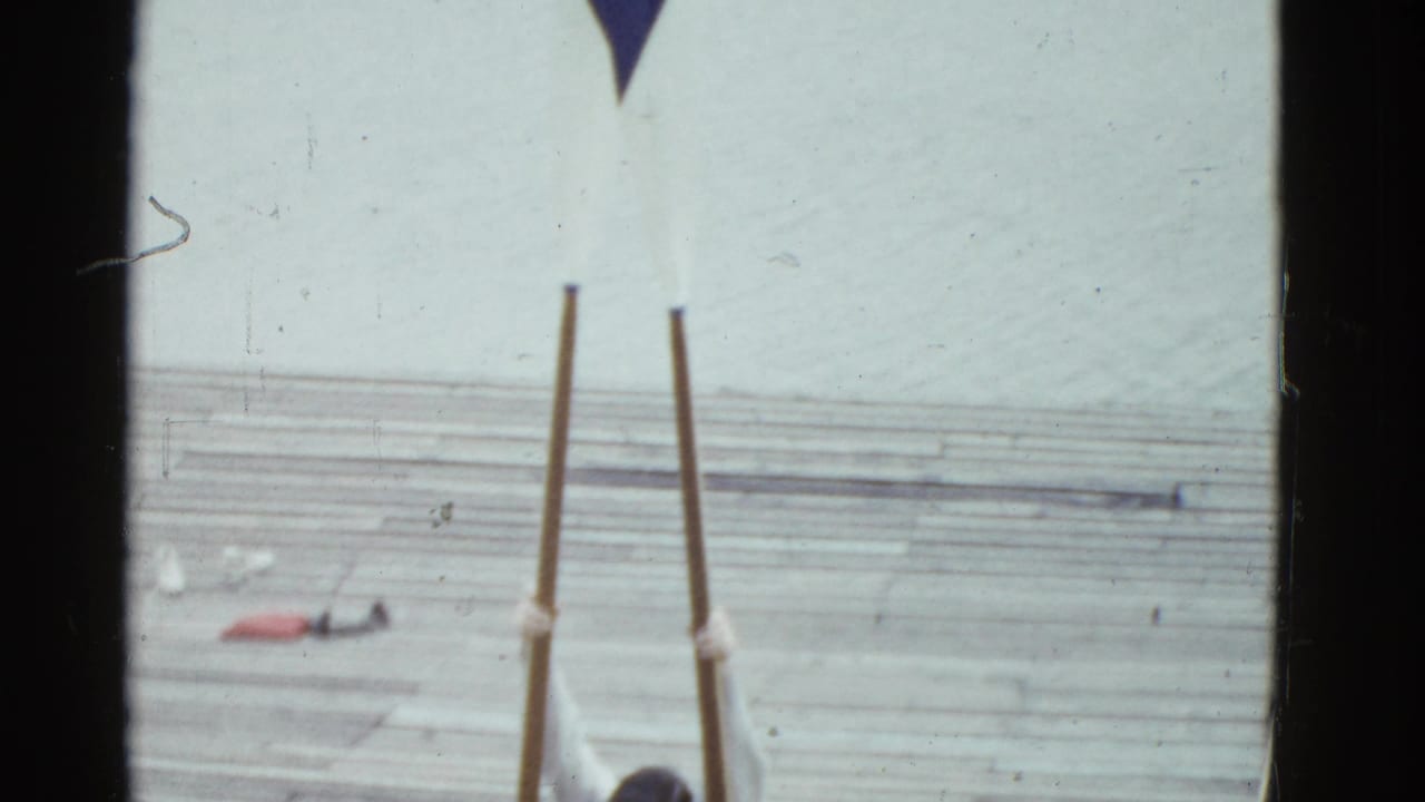 Long oars stand upright on a wooden dock beside a partial view of a man.