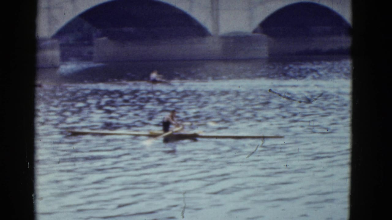Single scull rower on a river with arched bridge spans in the background.