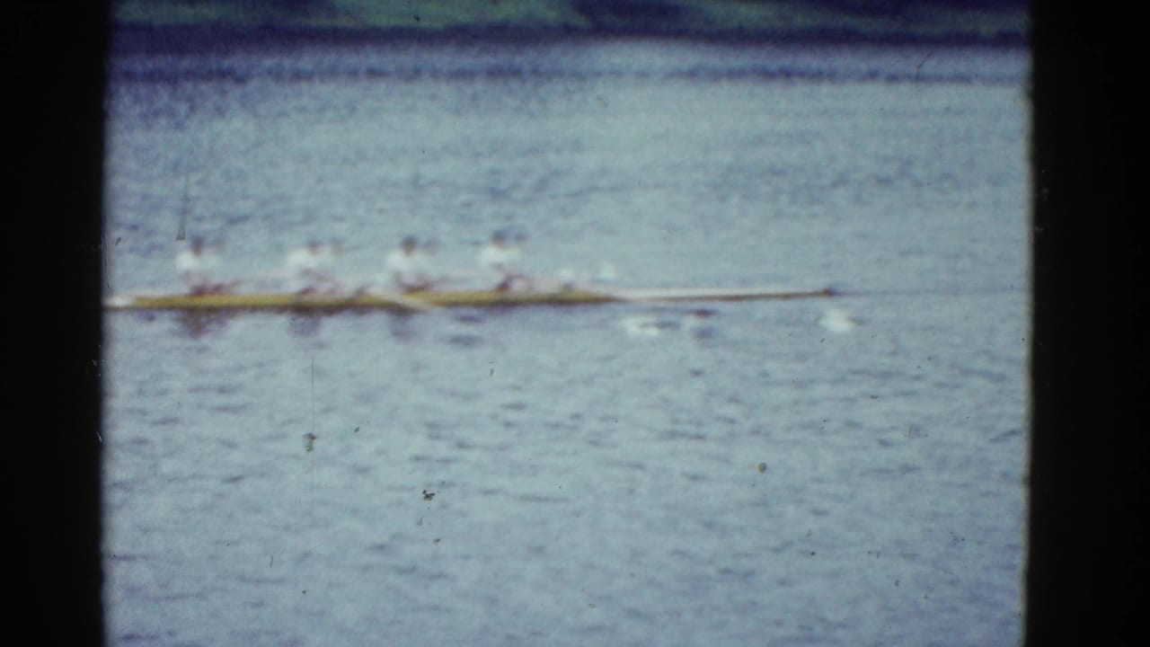 Distant rowers in a long racing shell move across rippling water.
