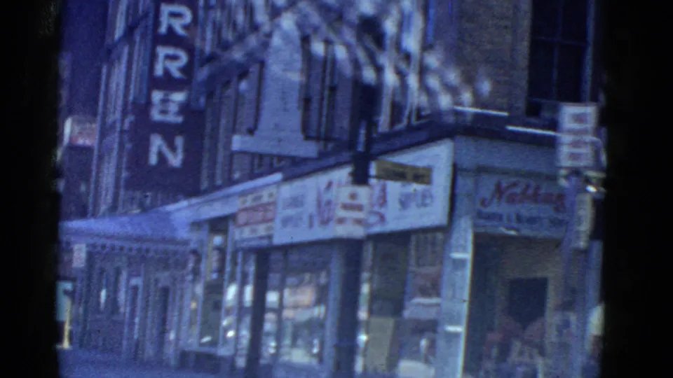 1975 Boston street frame showing Hotel Warren letters beside Nathan's Barber Shop and neighboring glass storefronts.