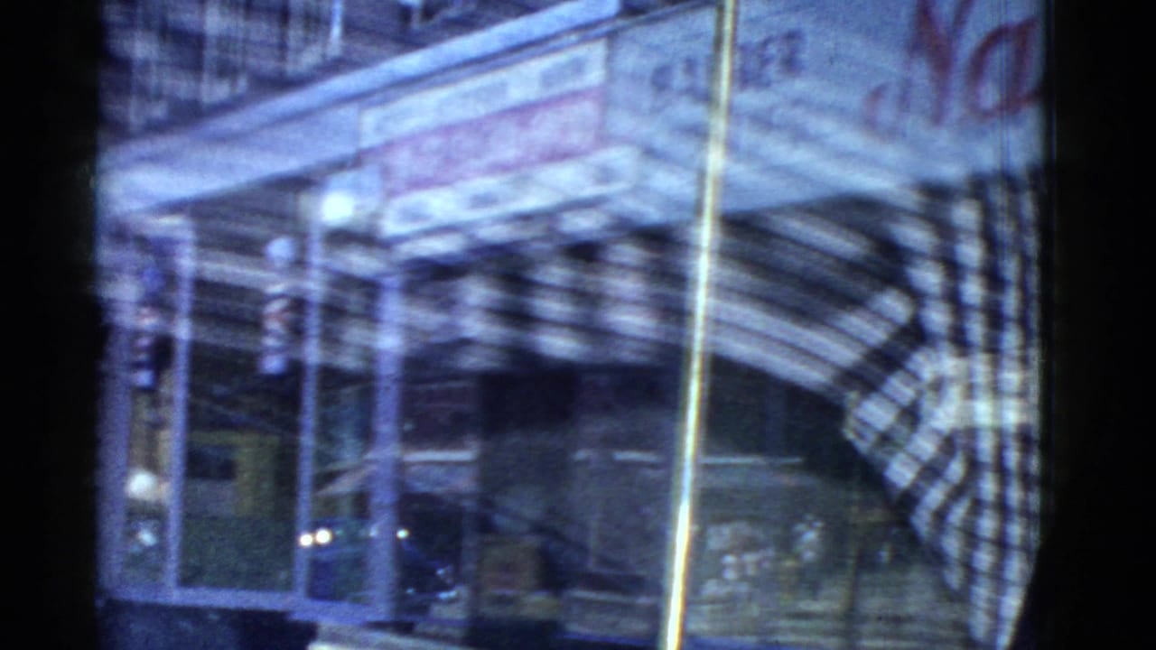 1975 Boston 8mm frame showing a blurred nighttime storefront and street reflections during an urban drive-by.