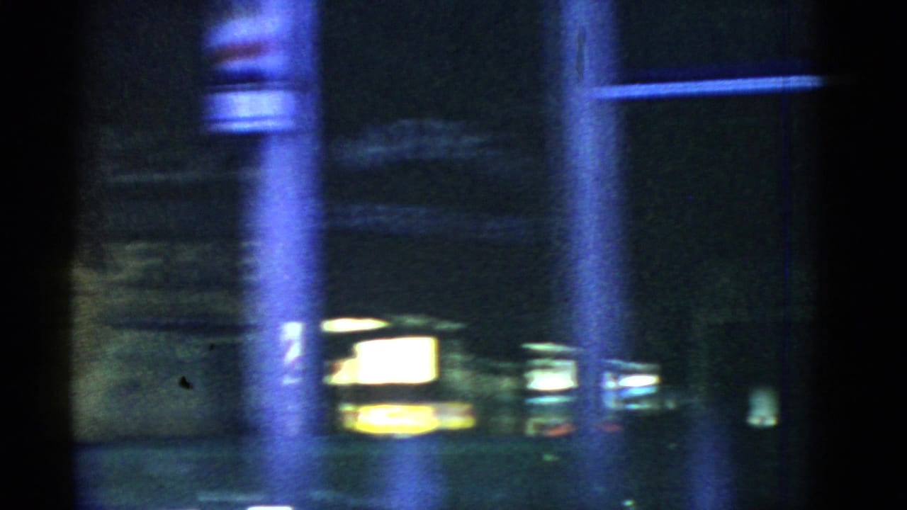 Dark street scene with poles and glowing signs through motion blur.