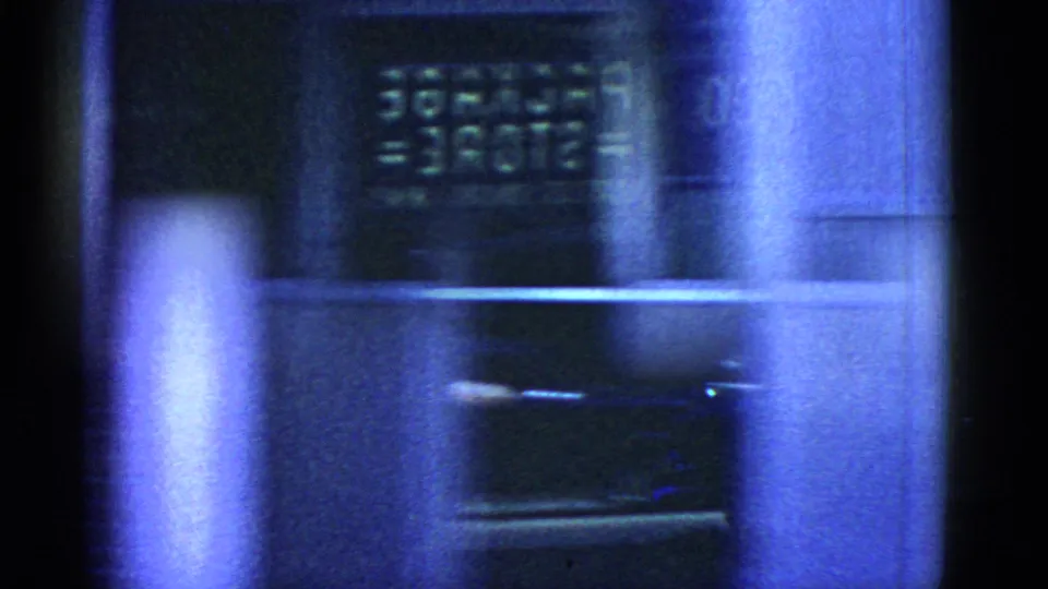 Blue-tinted 8mm night frame showing a storefront window with a visible MARTIN SUPPLIES sign during the Boston drive.