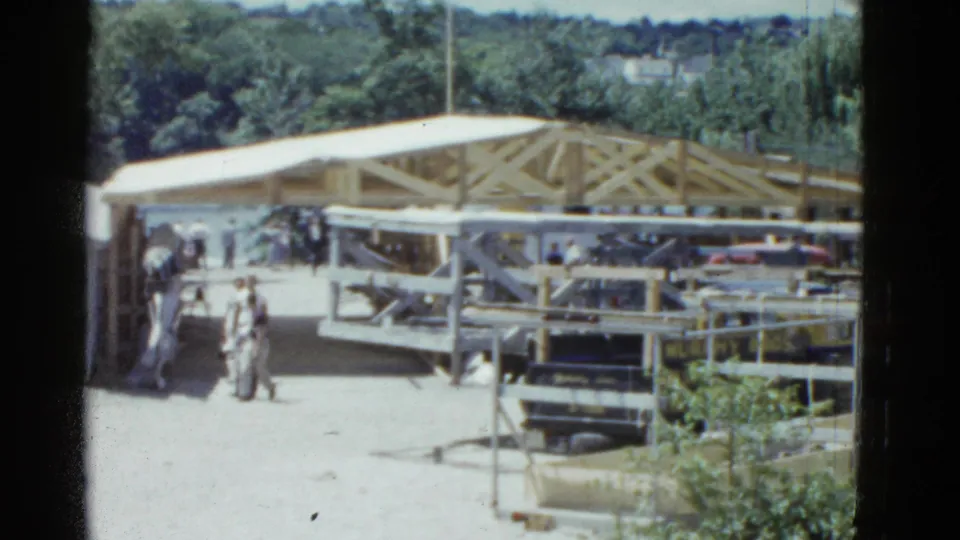 The final 1975 Massachusetts 8mm frame shows a wider view of the timber-framed construction site with people moving nearby.