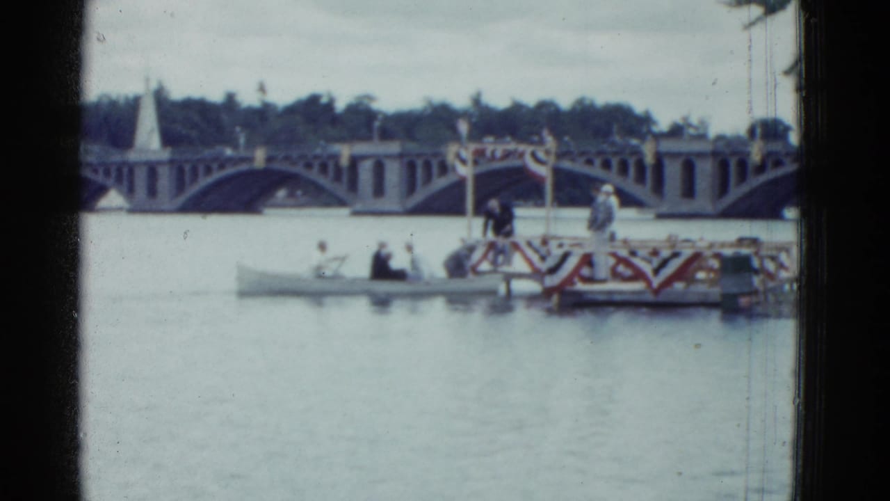 Decorated boat and small rowboat on a river in front of an arched bridge.