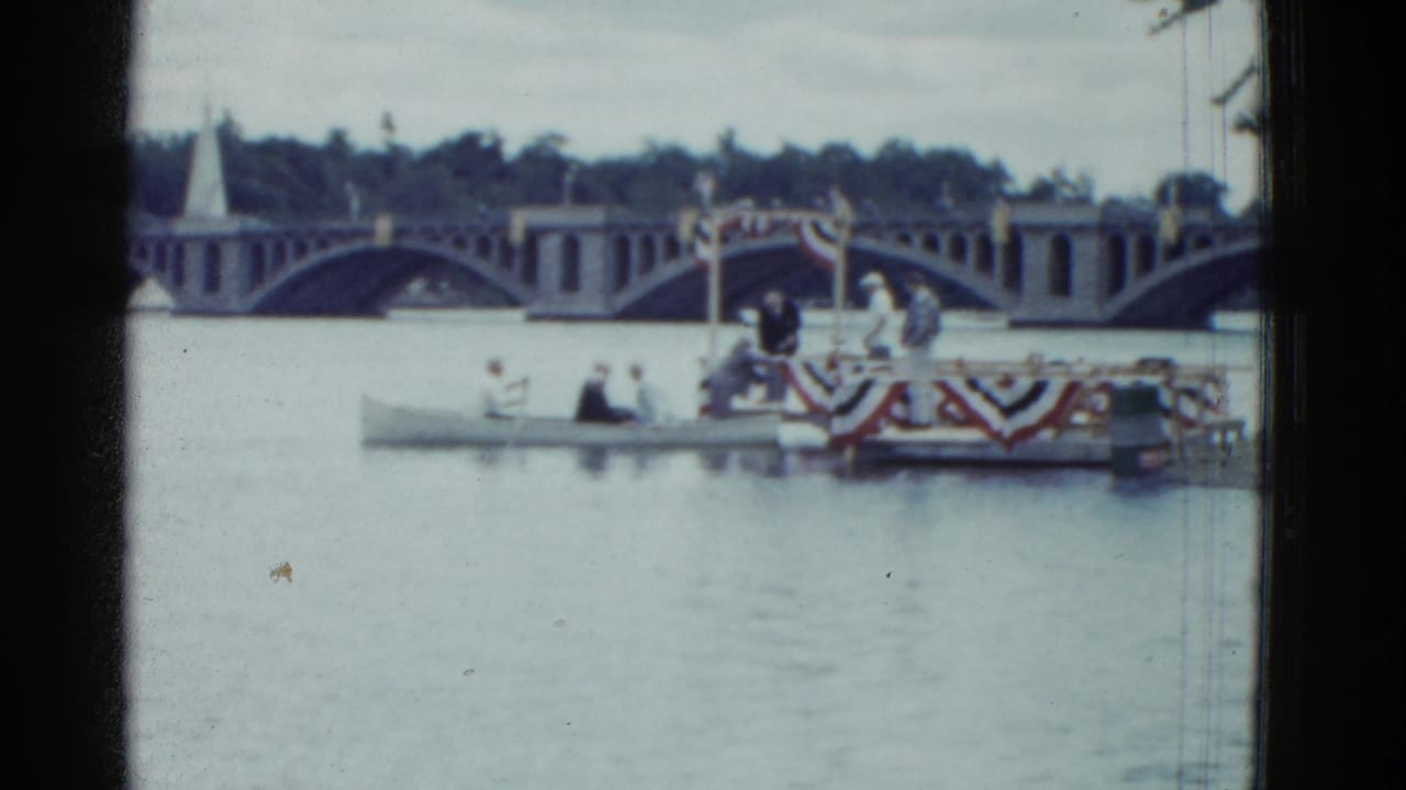 People in small boats near a decorated platform with an arched bridge behind them.