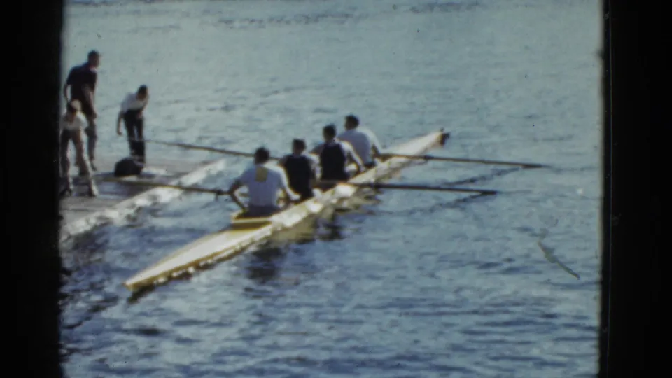 1975 Boston 8mm frame with a rowing shell pulled close to a wooden dock while the crew sits in formation.