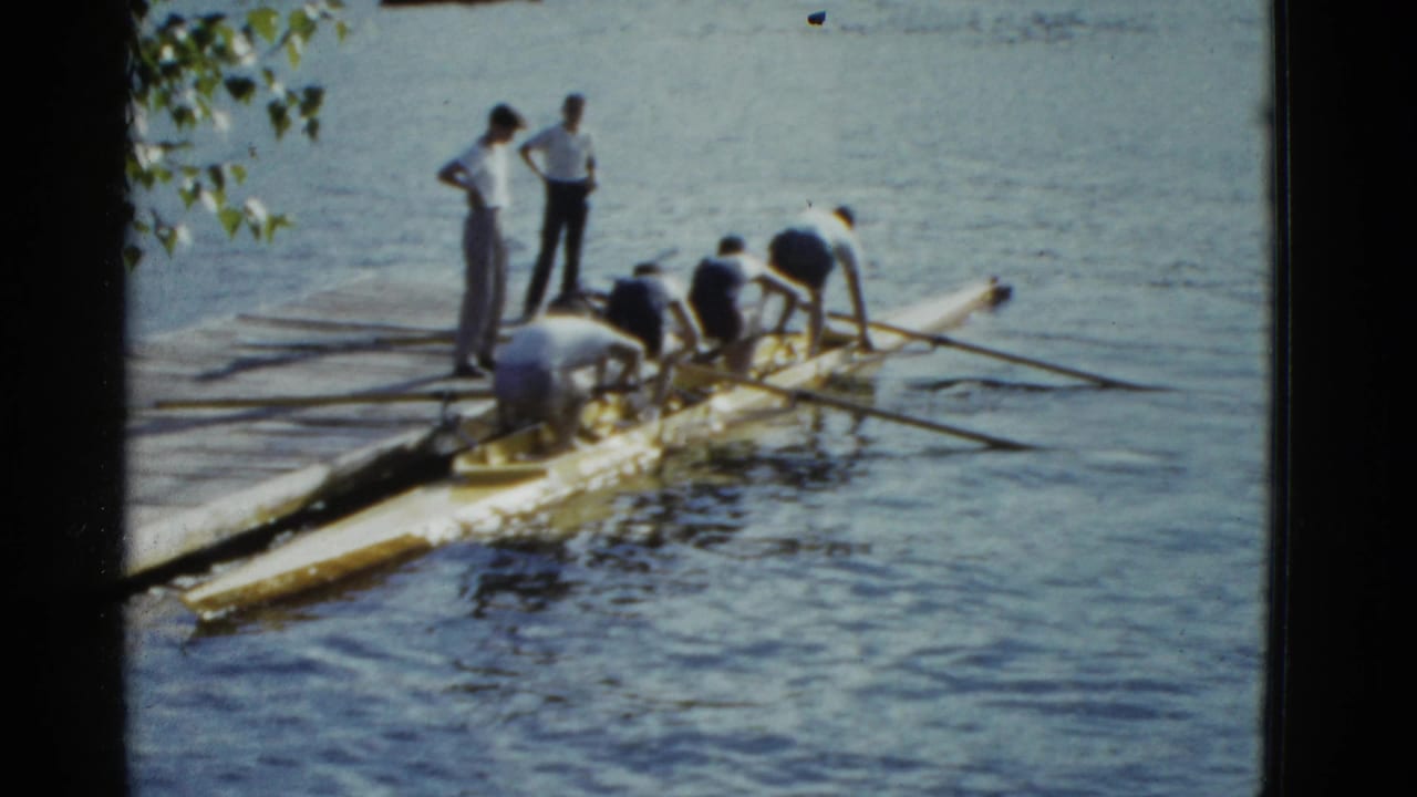 Men lean over a yellow rowing shell while two others stand on the dock.