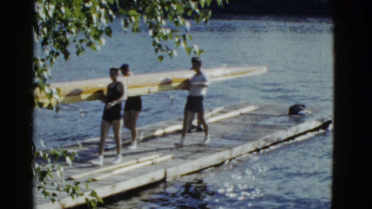 Rowers in athletic clothing carry a yellow racing shell along a wooden dock in the 1975 Boston clip.