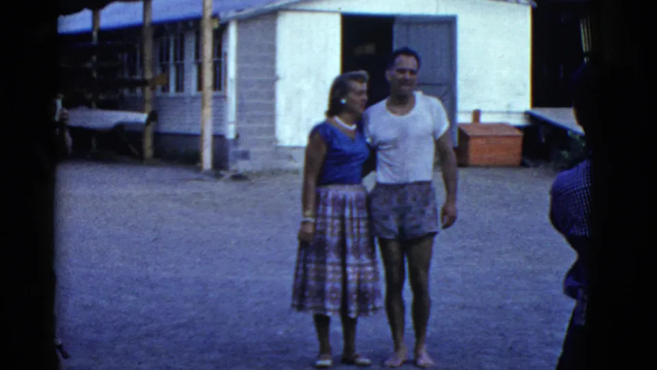 1975 Boston 8mm frame with a woman and man posing together in front of a building, filmed from a casual home-movie viewpoint.