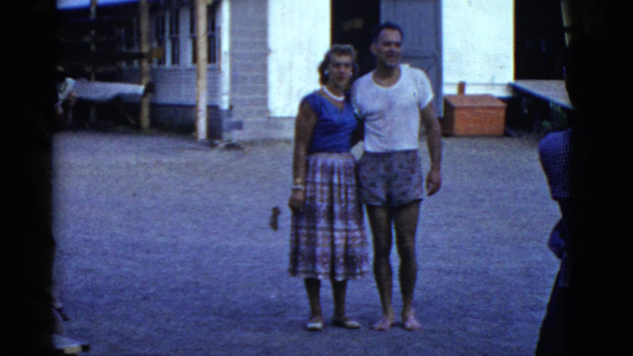 In this 1975 Boston-area home movie frame, a casually dressed woman and man stand together near a building at a lakeside retreat.