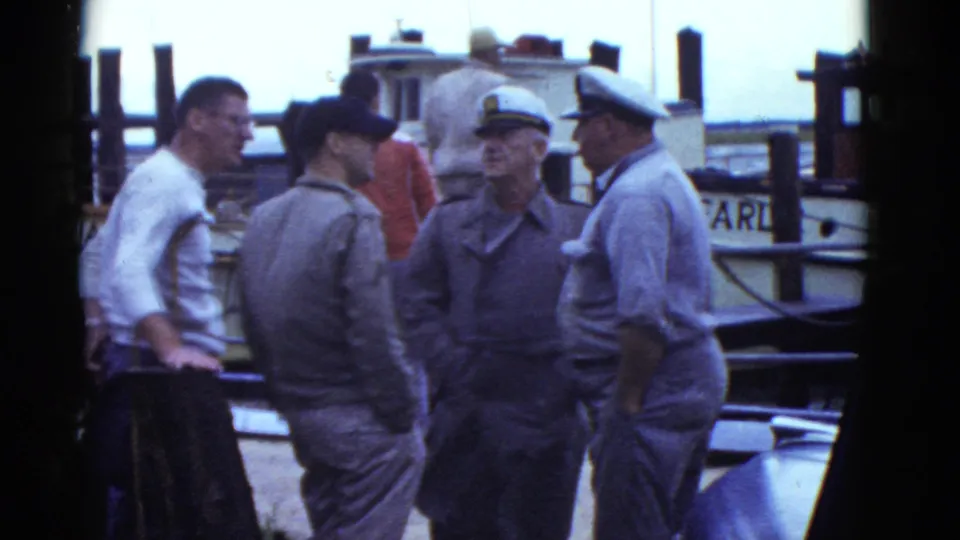 1975 Boston dock footage shows uniformed men and a man in suspenders gathered beside a small vessel.
