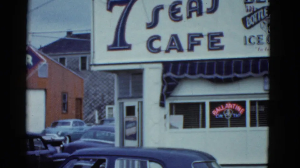 1975 Boston frame showing the Seven Seas Cafe exterior sign, nearby buildings, and parked vintage cars along the street.