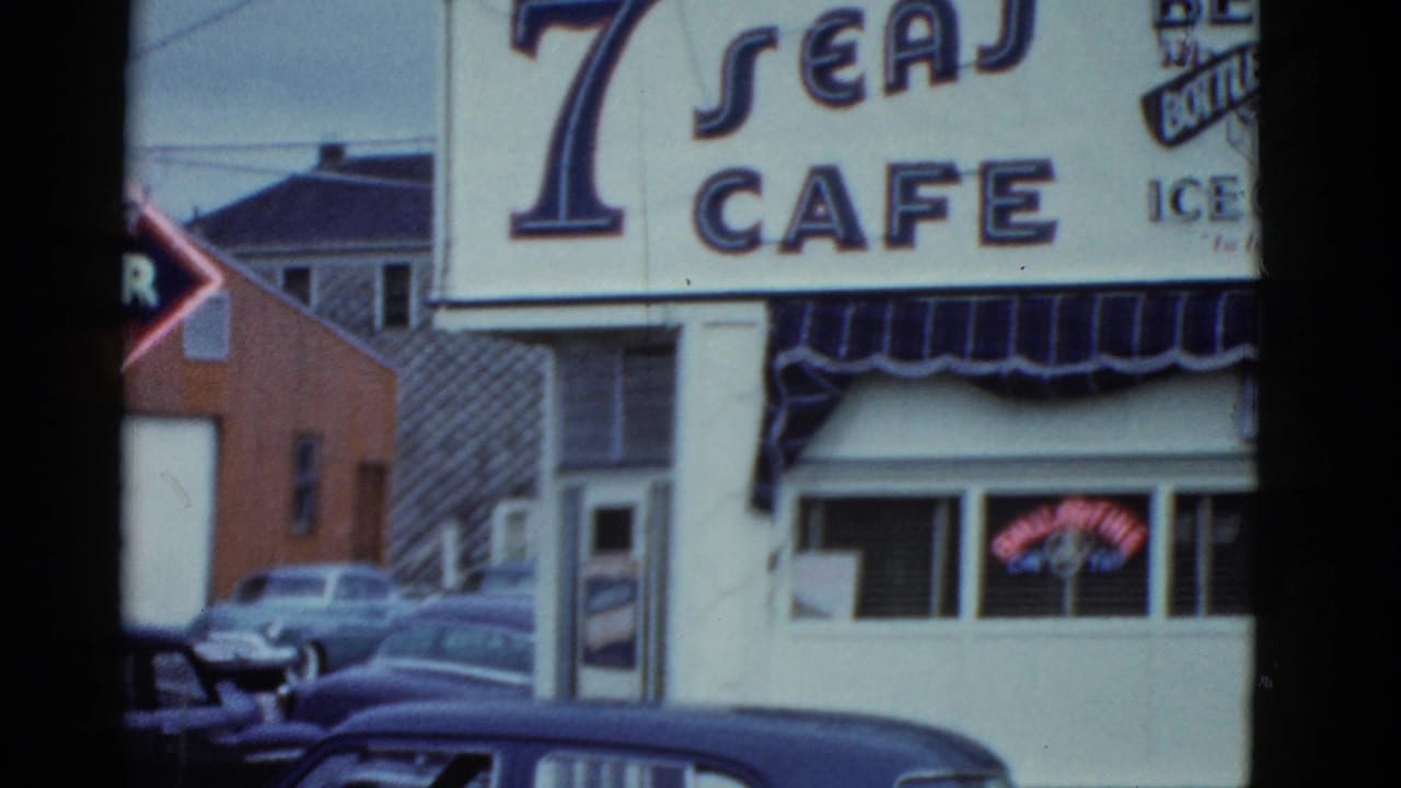 Boston 1975 street view of the 7 Seas Cafe exterior, with cropped sign lettering, awning, neon beer sign, and older cars.