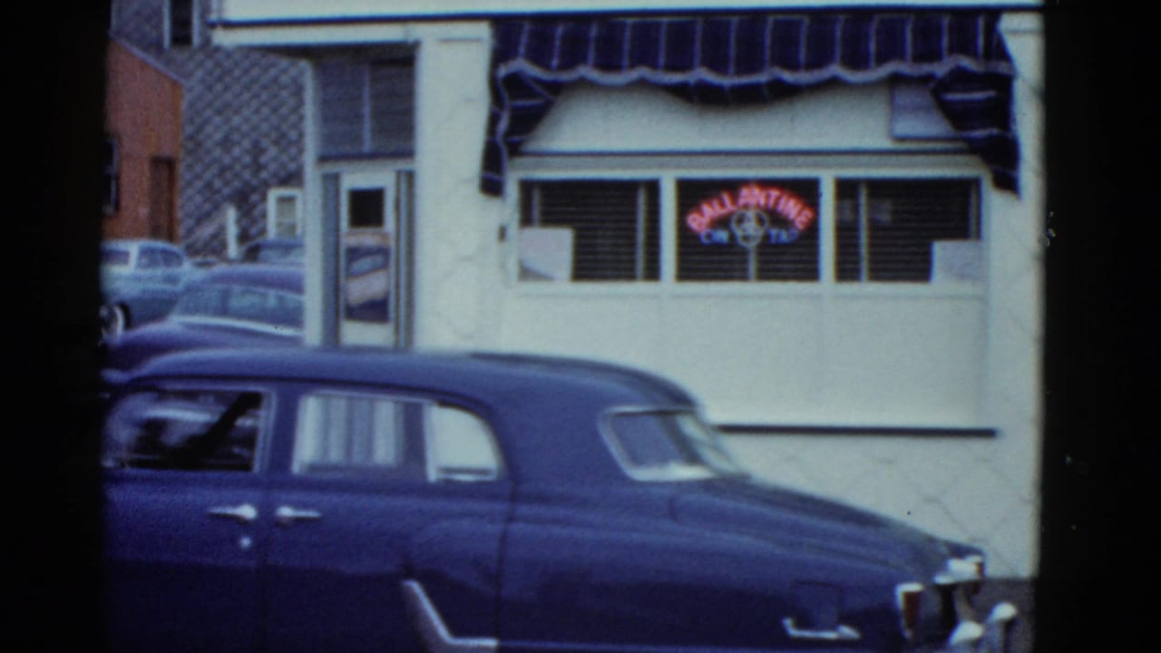Blue sedan parked in front of a storefront window with a neon sign and striped awning.