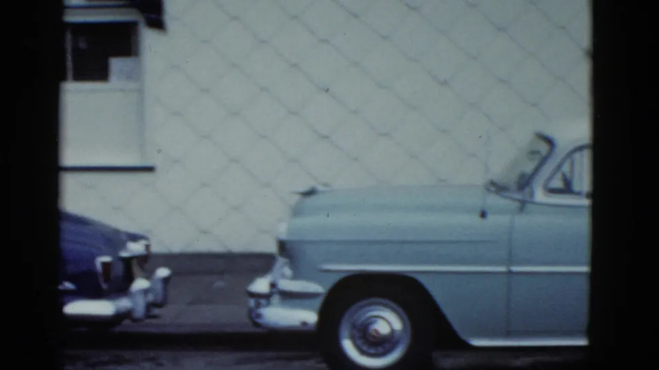 Turquoise mid-century car parked beside a blue sedan along a white building wall in 1975 Boston-area footage.